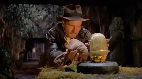 Which movie features this iconic scene with Harrison Ford replacing a treasure with a sandbag?